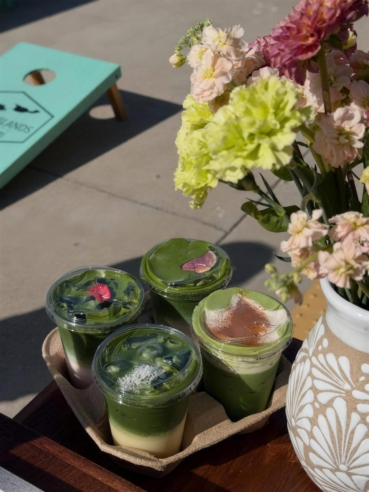Layered matcha drinks and flowers on a wooden table